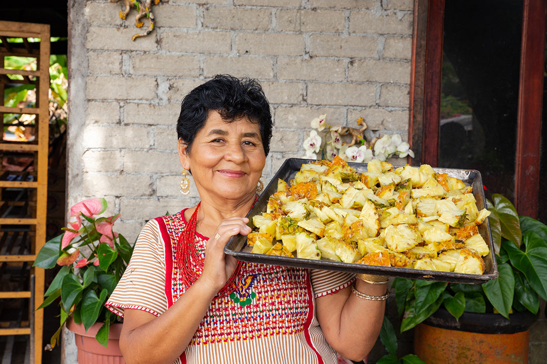 Doña Hilda Figueroa sostiene un recipiente con curado de piña tradicional, rodeada de platanales en Santa María Zacatepec.