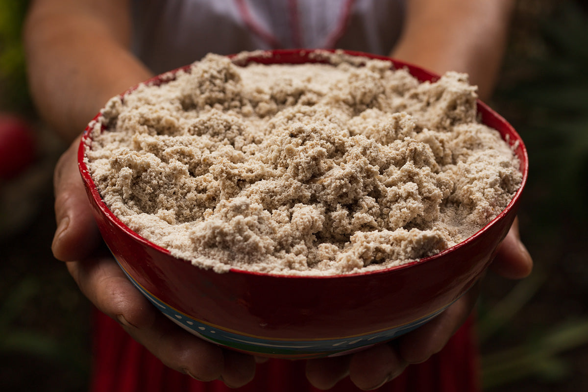 Persona sostiene una jícara roja llena de masa espumosa de tejate, bebida tradicional hecha con maíz y cacao en Oaxaca.